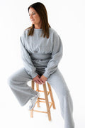 Woman sitting on a stool wearing a gray tracksuit against a white background